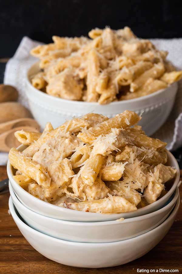A white bowl full of this Crock Pot Olive Garden Chicken Alfredo Pasta on a wooden board with another bowl of chicken pasta behind it. 
