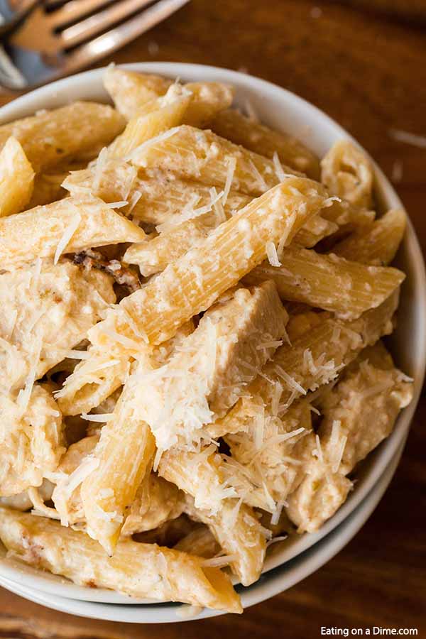 Close up of a white bowl full of this Crock Pot Olive Garden Chicken Alfredo Pasta on a wooden board. 

