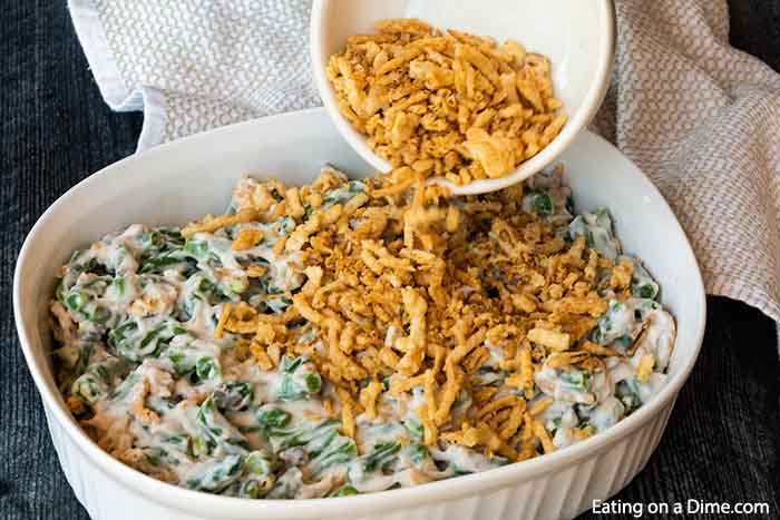 Close up image of green bean casserole in process with the french fried onions being placed on top. 