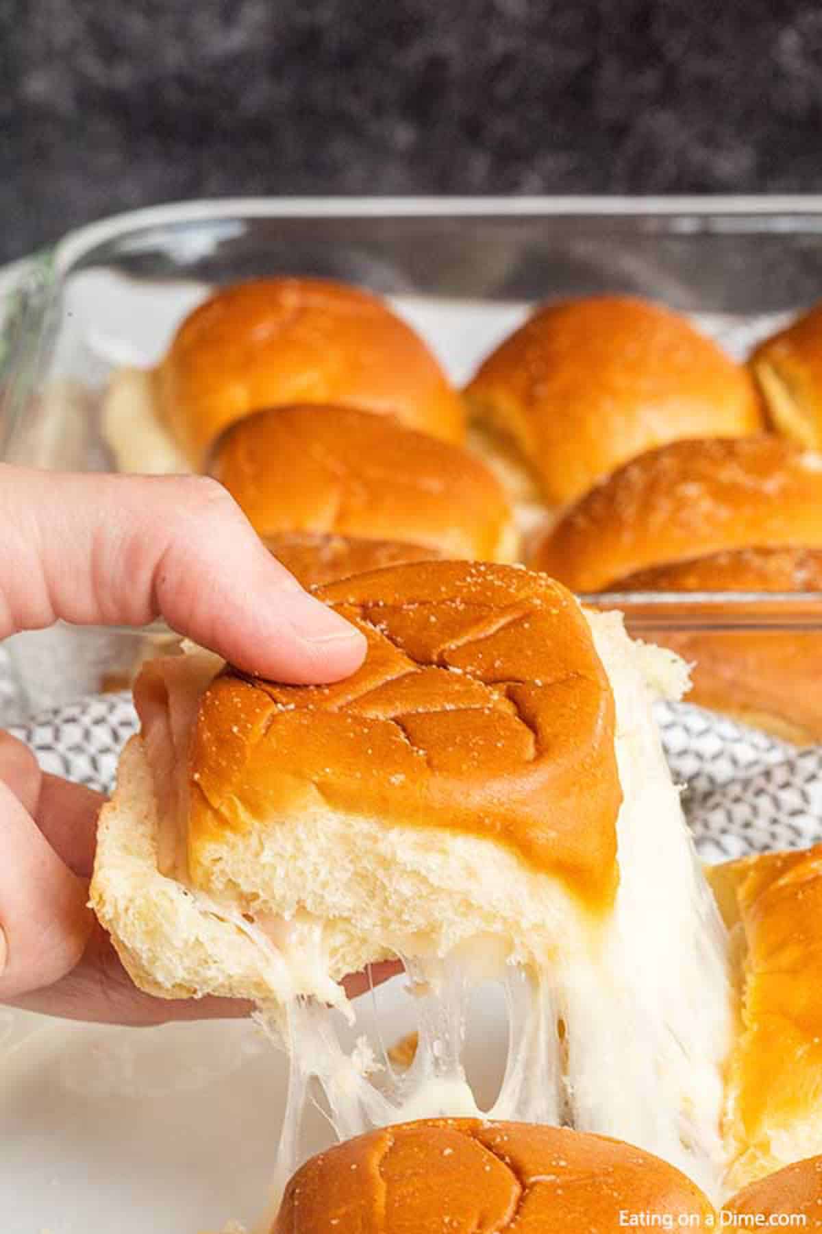 These quick and easy Hawaiian turkey and cheese sliders are the best for feeding a crowd! Hawaiian roll turkey sliders are our go to recipe for party food! Turkey sliders in a baking dish in the background with one slider being pulled from the rest with melted cheese
