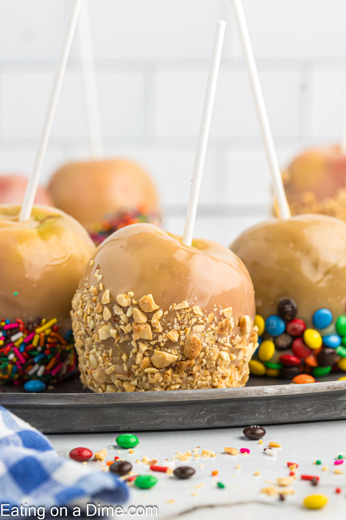 Close up image of caramel apples with chopped nuts, sprinkles and mini m&m's on a platter