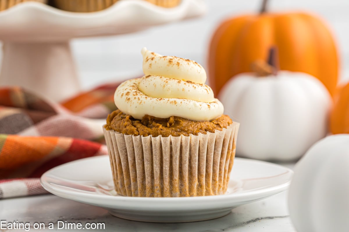 Pumpkin Cupcake on a plate topped with cream cheese frosting with pumpkin decorations in the background
