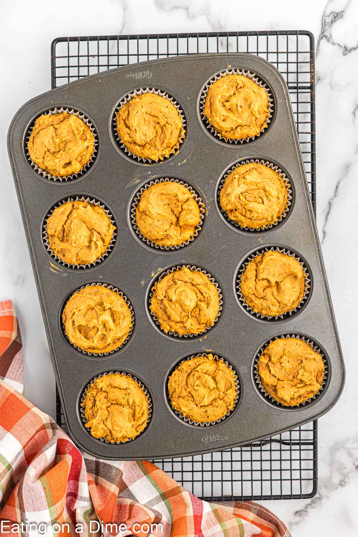 Baked pumpkin cupcakes in the muffin tin cooling on the rack