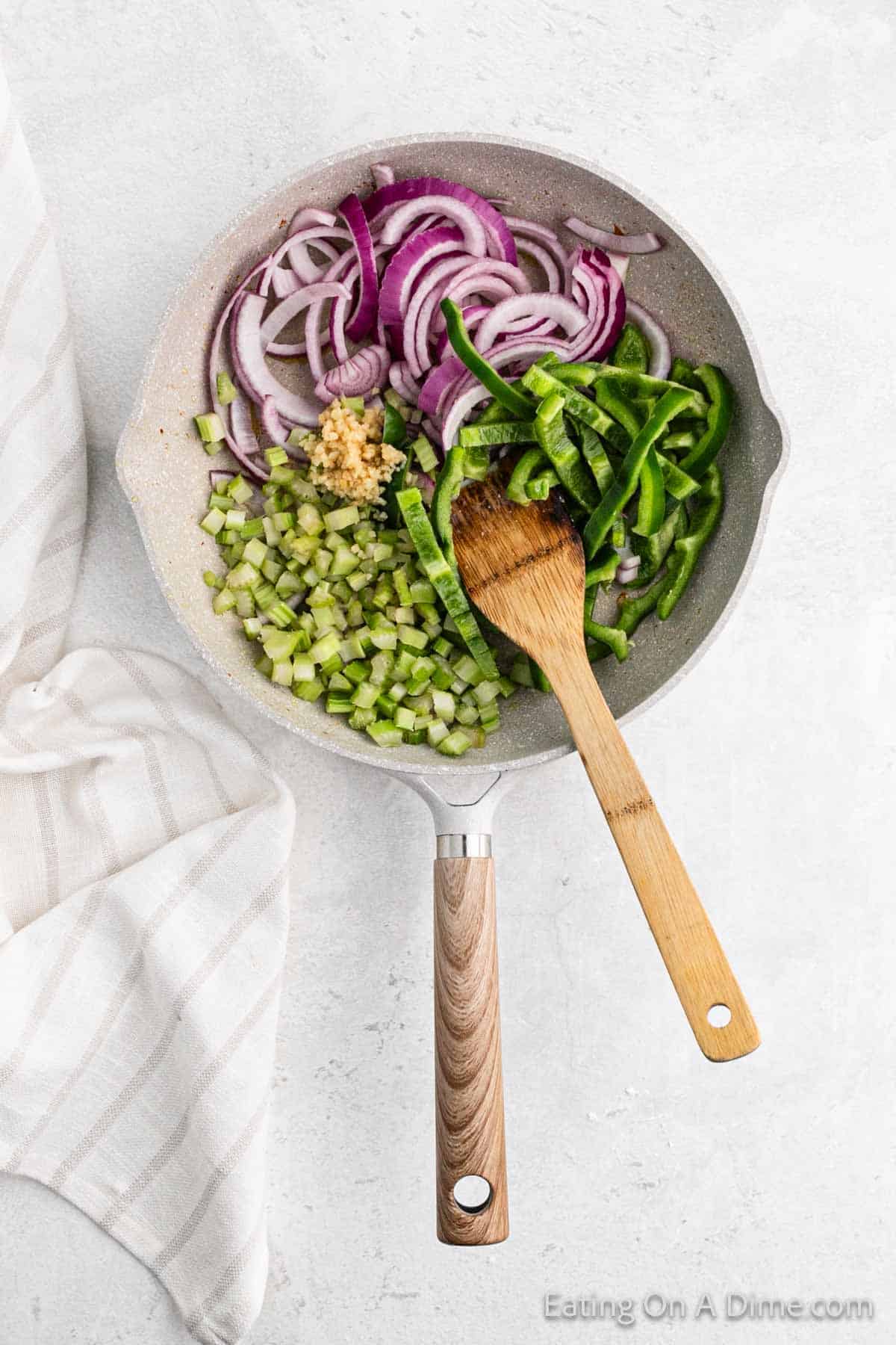 Cooking red onions, green bell peppers, celery and minced garlic in a large skillet with a wooden spoon