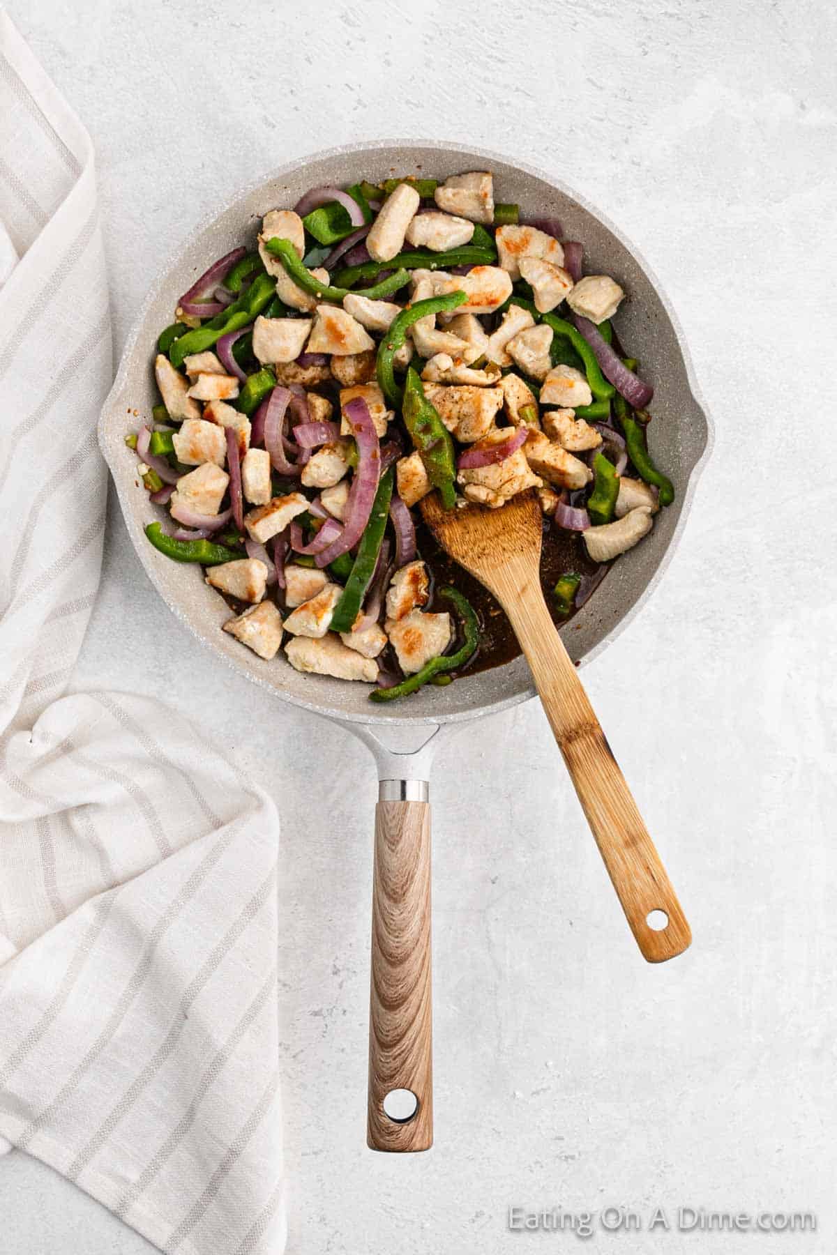 Placing the cooked diced chicken and vegetables in a large skillet with a wooden spoon