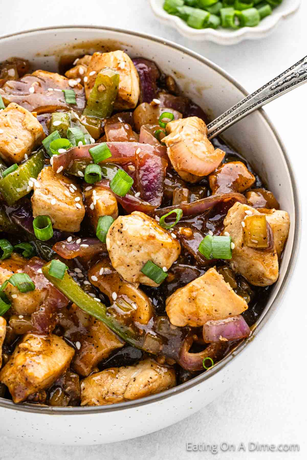 Black Pepper Chicken in a large bowl with cooked onions in a sauce topped with sesame seeds and chopped green onions