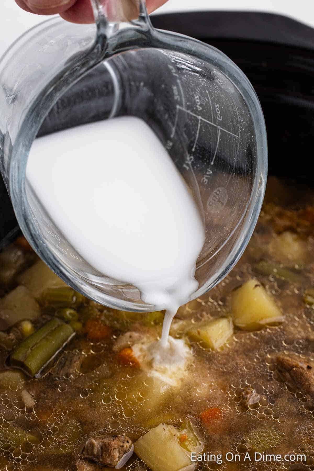 Pouring cream in the slow cooker with the potatoes, green beans and stew meat