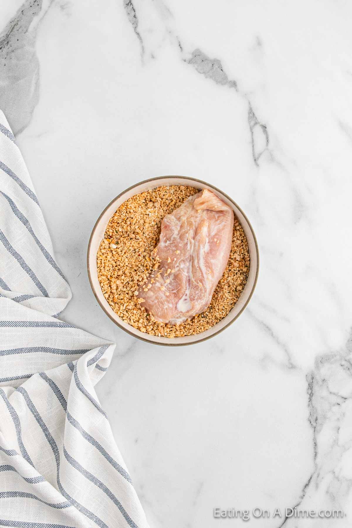 Placing the chicken breast in the bowl of the breadcrumbs mixture