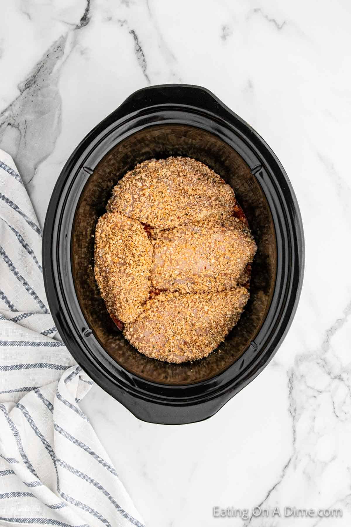 Placing the coated chicken breast in the slow cooker