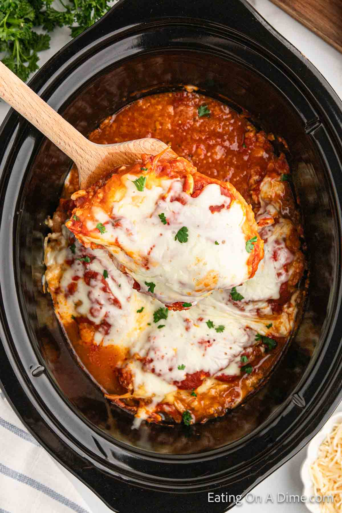 Cooked chicken parmesan in the slow cooker with a serving on a wooden spoon
