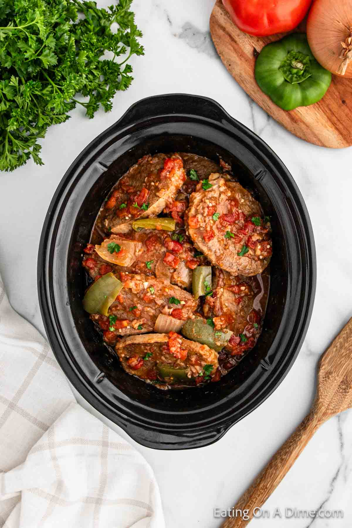 Cooked swiss steak covered in sauce with bell peppers and tomatoes in the slow cooker