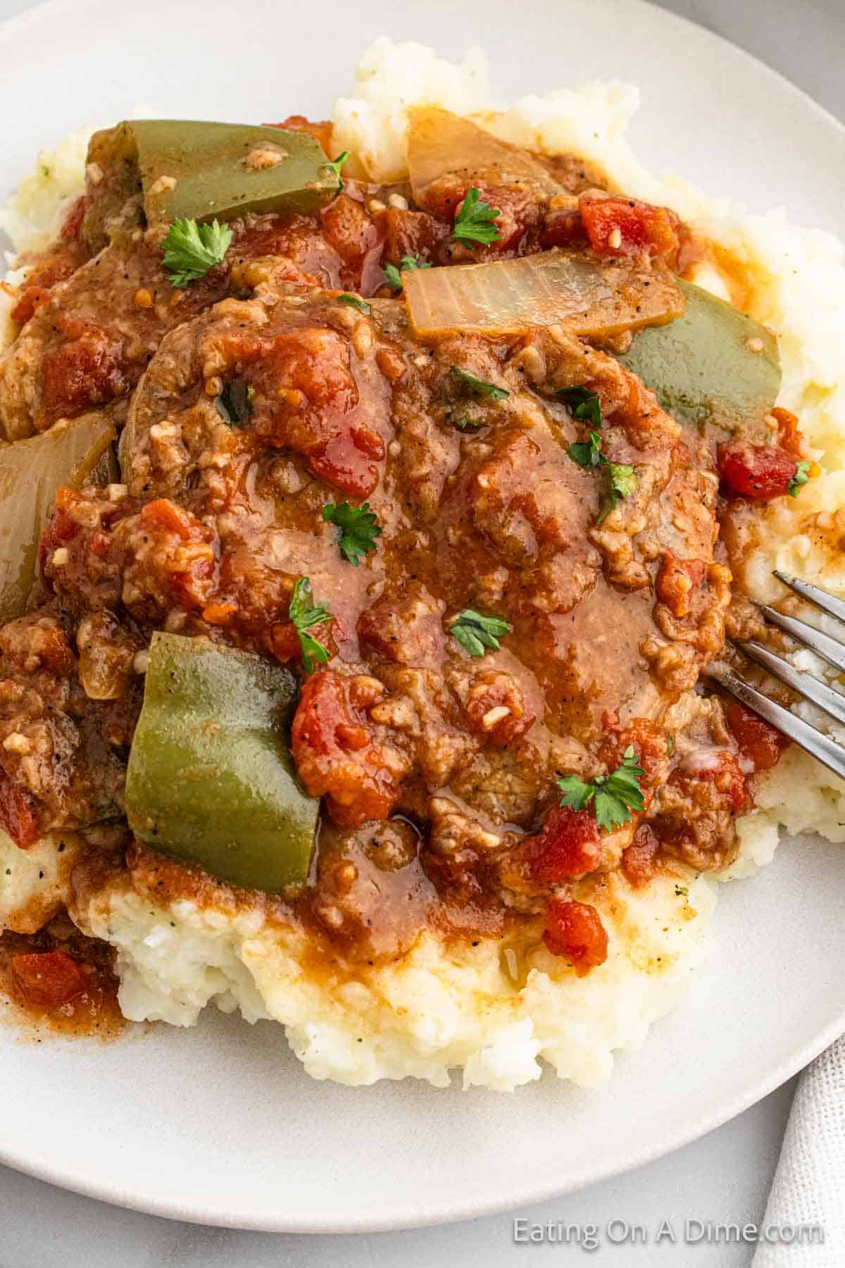 A serving of swiss steak and tomato sauce on mashed potatoes 