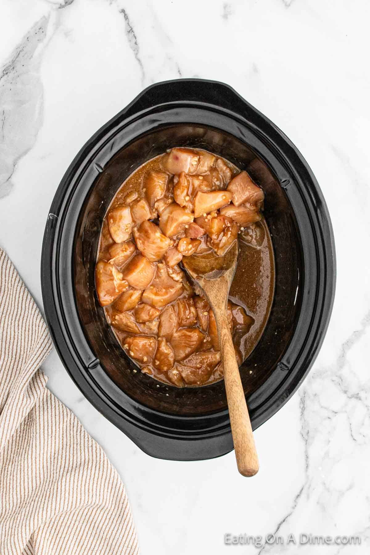 Combining the chicken into the sauce in the slow cooker with a wooden spoon