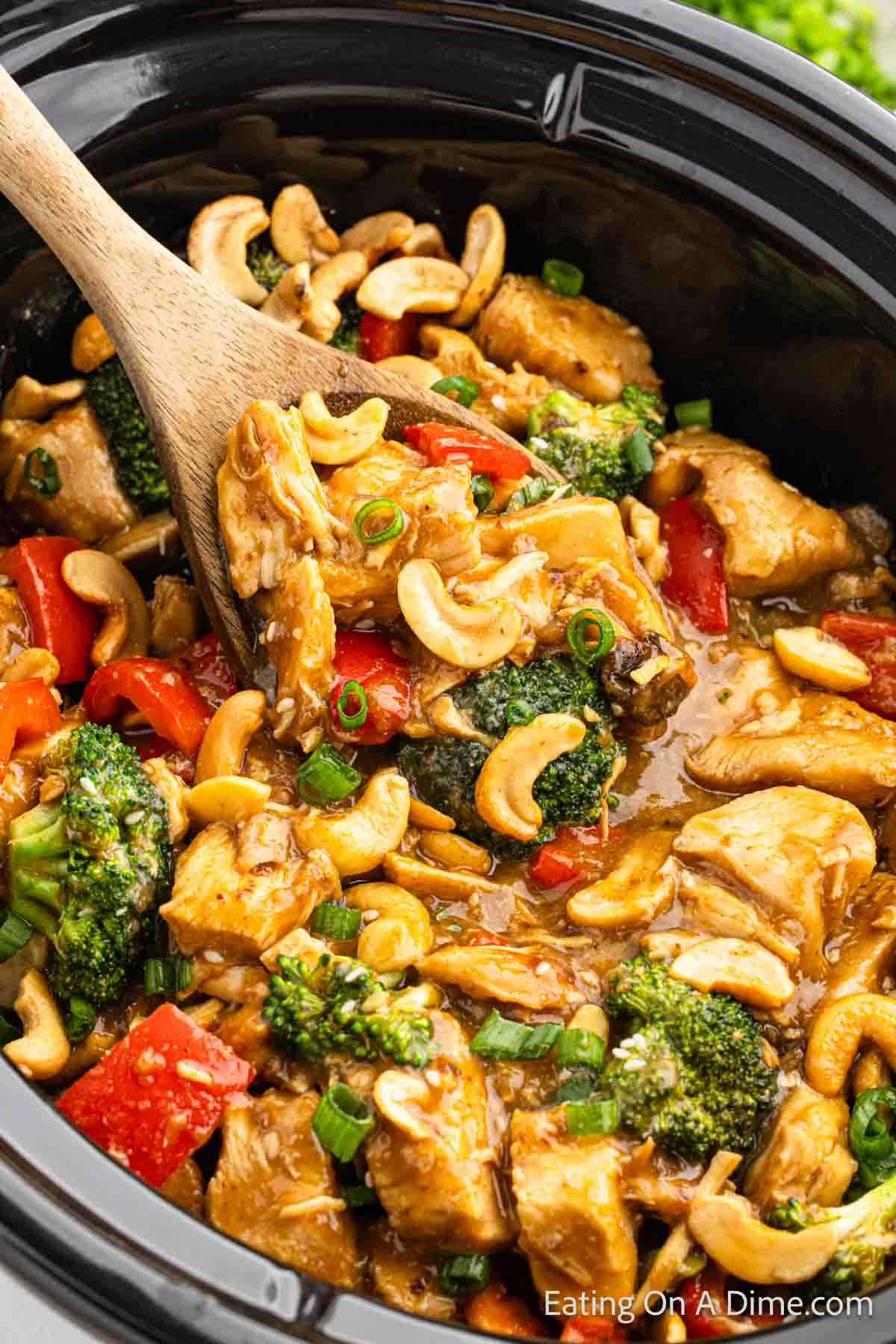 Cashew chicken in the slow cooker with a wooden spoon