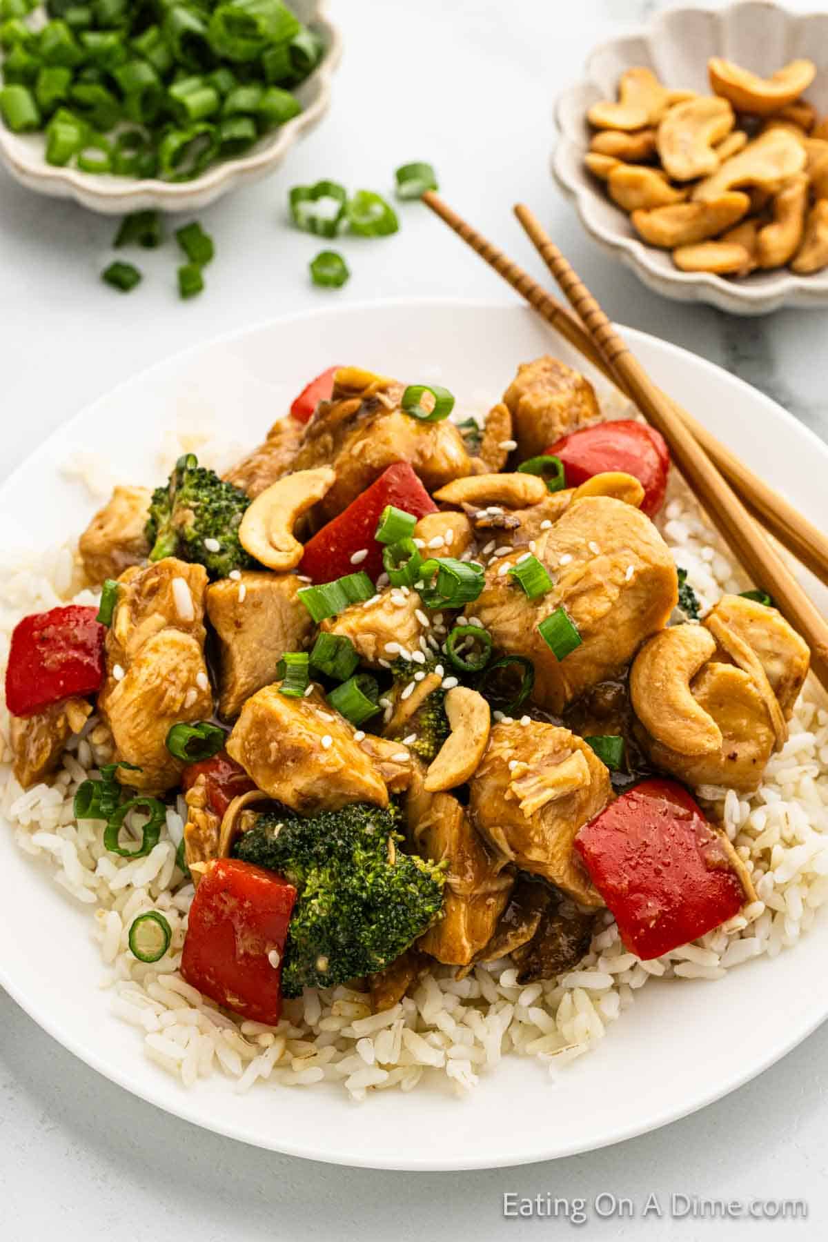 Cashew Chicken topped on white rice on a plate with chopsticks