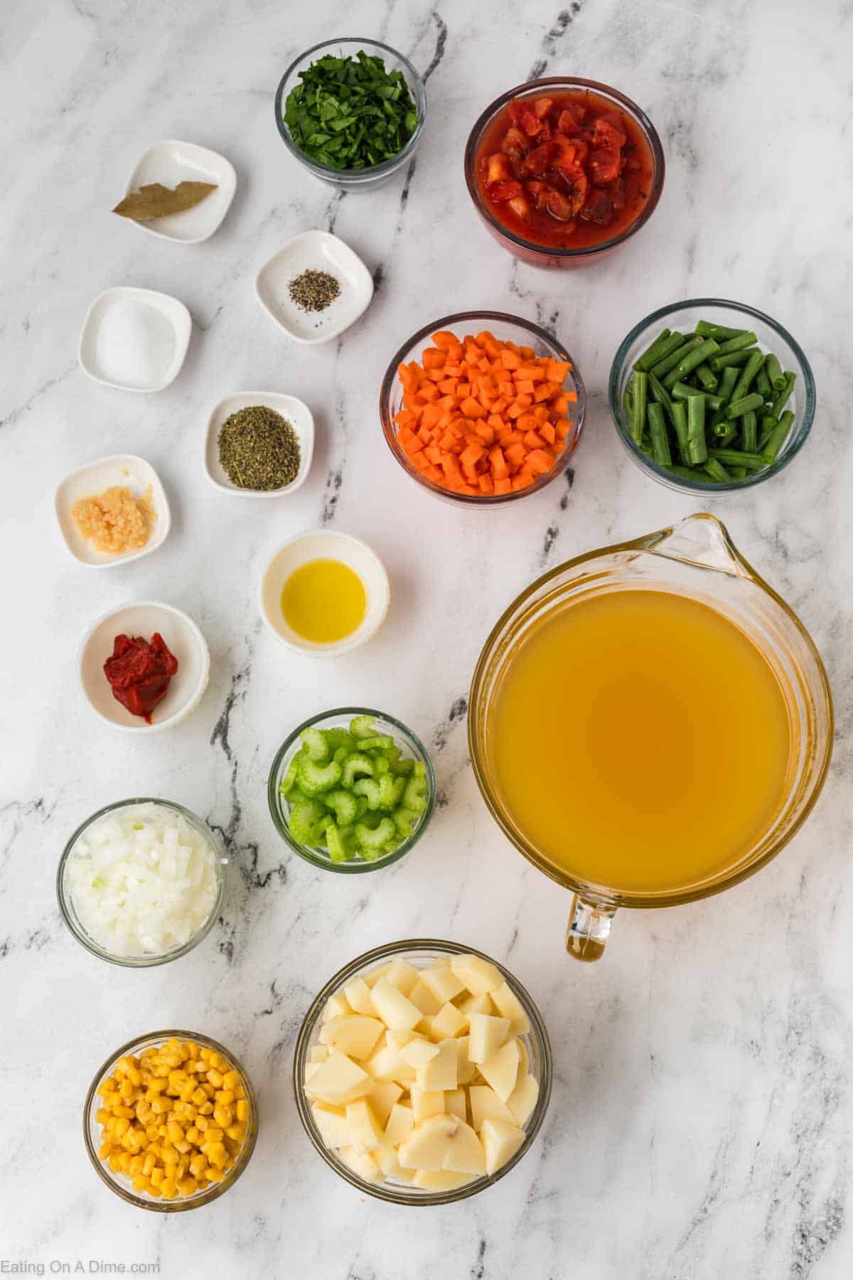 Various Instant Pot Vegetable Soup ingredients are arranged on a white marble surface, including chopped potatoes, celery, onions, carrots, green beans, corn, diced tomatoes, seasonings, herbs, oil, and a large container of broth.