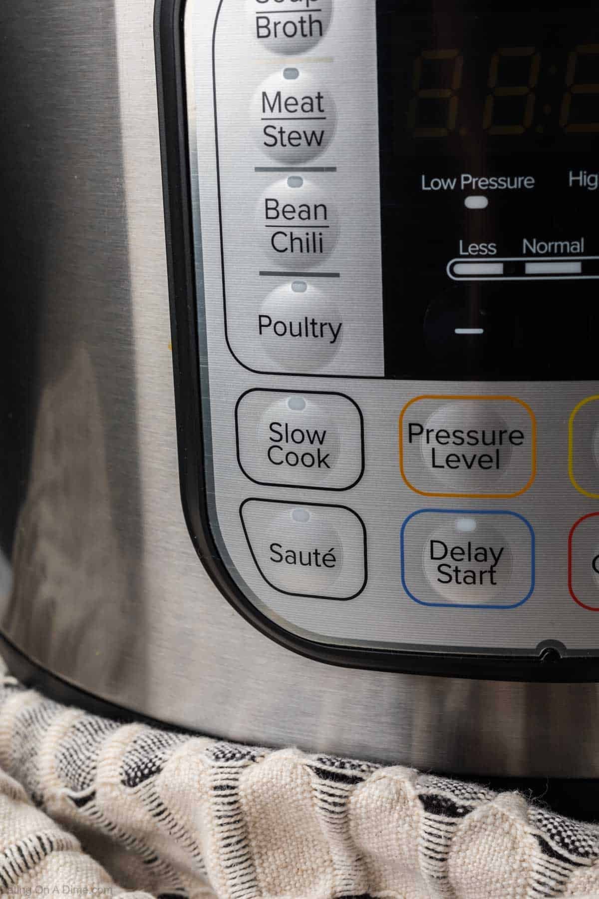Close-up of an electric pressure cooker control panel, featuring buttons for broth, meat stew, bean chili, poultry, slow cook, sauté, pressure level, and delay start—perfect for making Instant Pot Vegetable Soup. A striped cloth sits beneath the cooker.