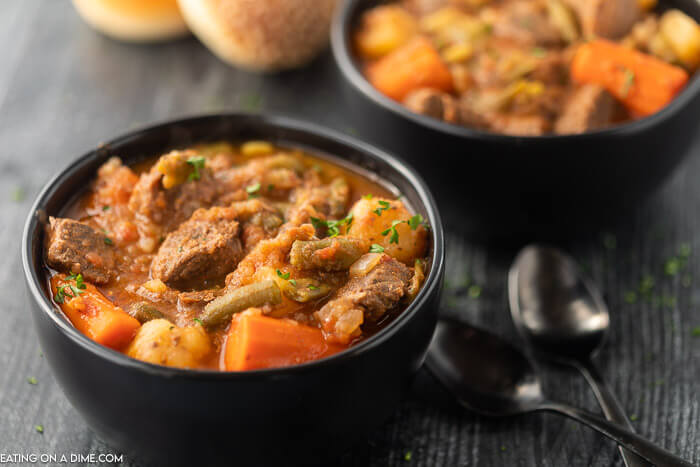 Close up image of two black bowls of beef stew with two spoons.