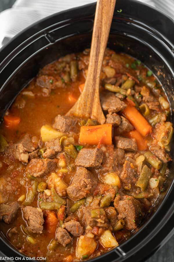 Close up image of crock pot beef stew with a wooden spoon. 