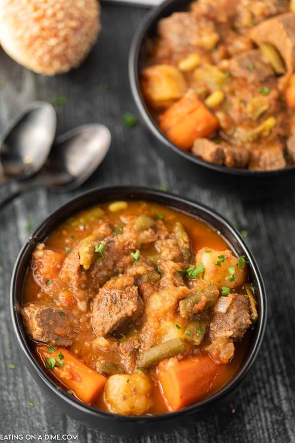 Close up image of a black bowl of beef stew with two spoons. 