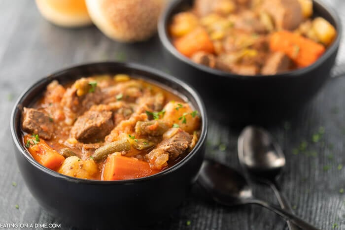 Close up image of a two black bowls of beef stew with two spoons. 