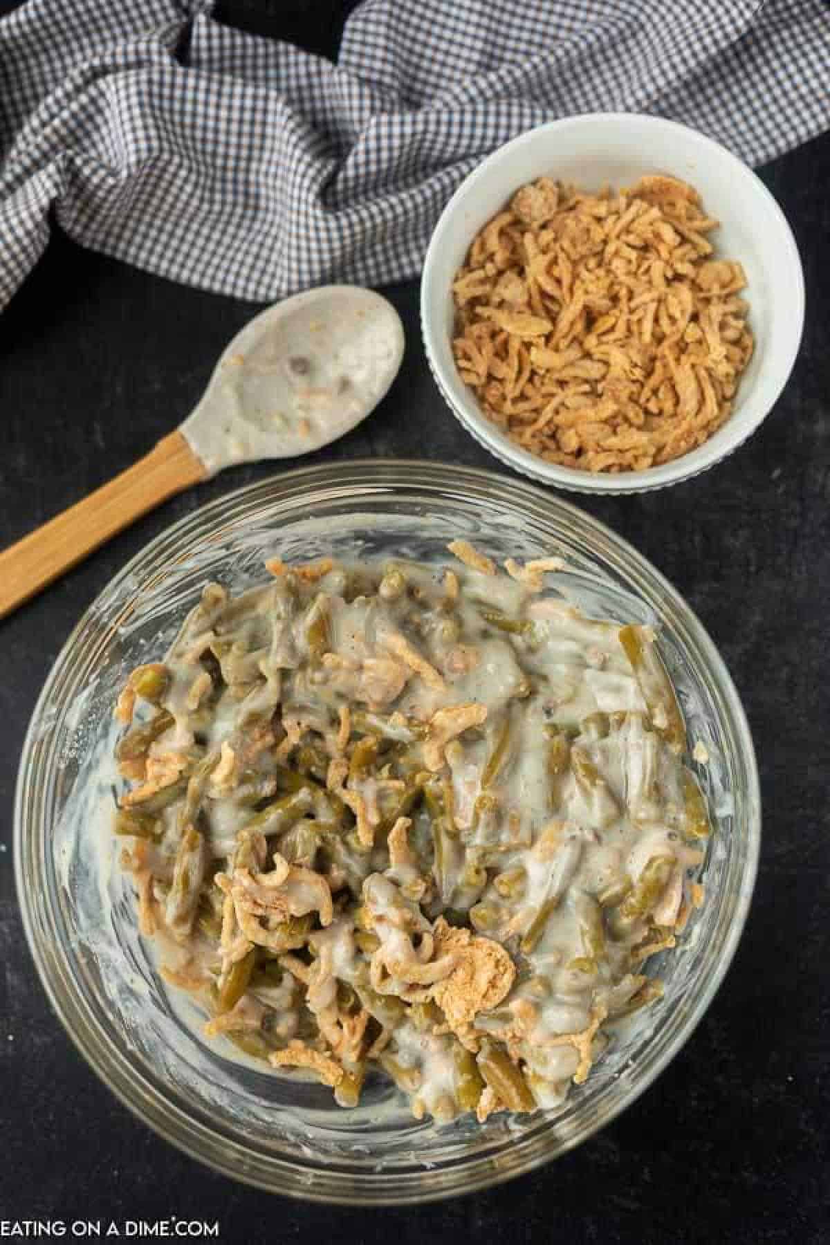 Green beans added to the cream of mushroom mixture in a bowl with the French fried onions nearby.