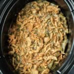 Crockpot Green Bean Casserole topped with crispy fried onions, featuring a creamy mixture of green beans beneath a golden, crunchy layer—all slow-cooked to perfection.