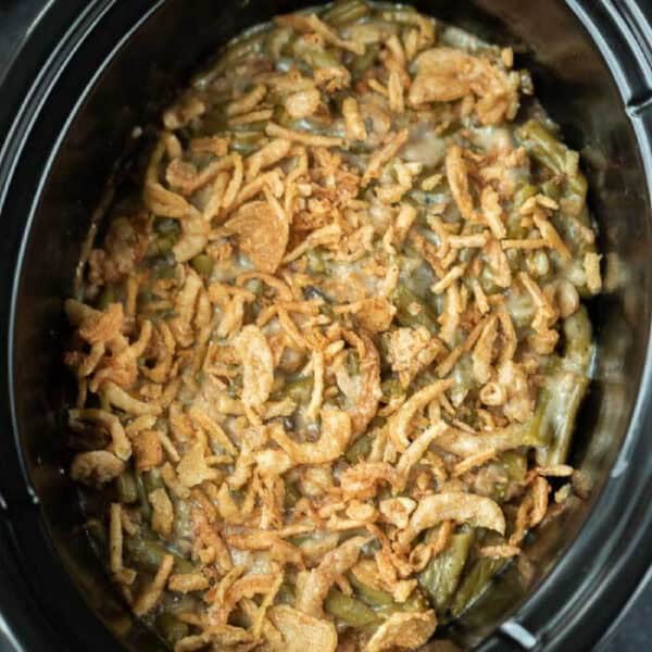 Crockpot Green Bean Casserole topped with crispy fried onions, featuring a creamy mixture of green beans beneath a golden, crunchy layer—all slow-cooked to perfection.