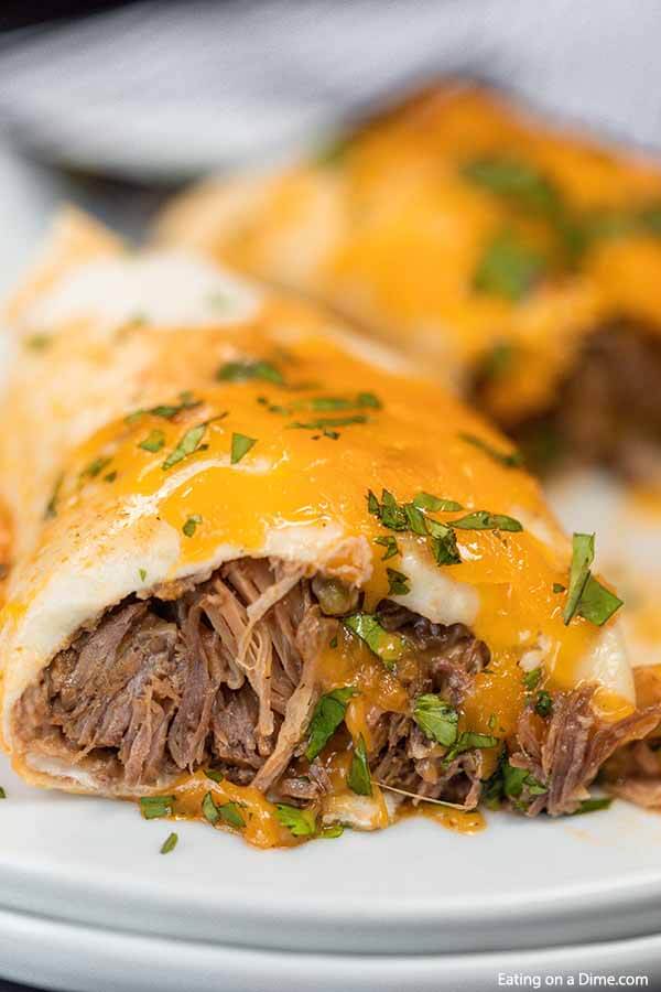 Crock pot smothered burritos will be a family favorite.  Tender beef smothered with cheese and more make this green chili recipe so flavorful. The crockpot makes it simple and easy. This crock pot Mexican recipe for smothered burritos has the best green sauce. #eatingonadime #crockpotsmotheredburritos #slowcooker
