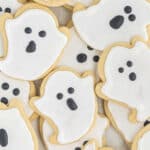 A pile of Ghost Cookies decorated to look like spooky ghosts with white icing and black icing for eyes and mouth.