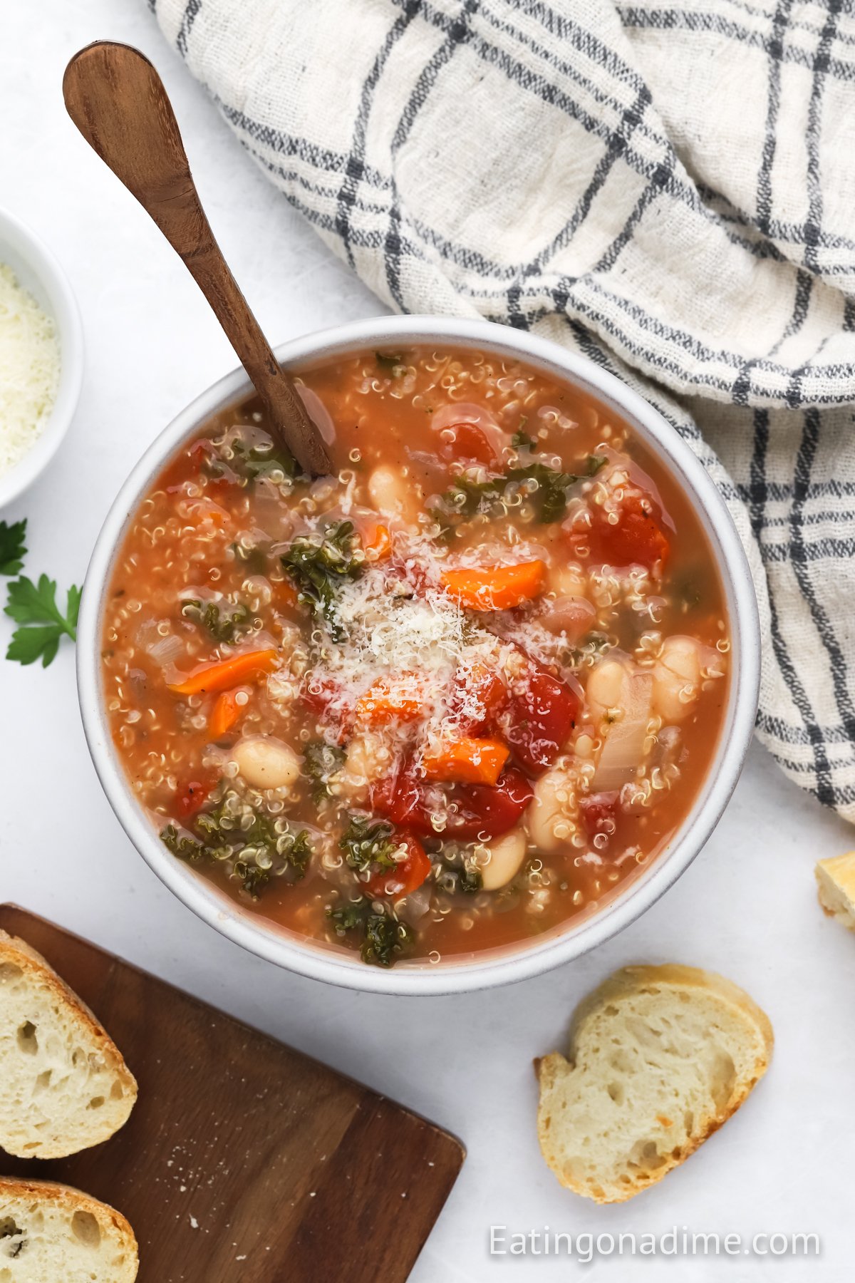 Quinoa Soup in a white bowl with a spoon. Topped with shredded parmesan cheese