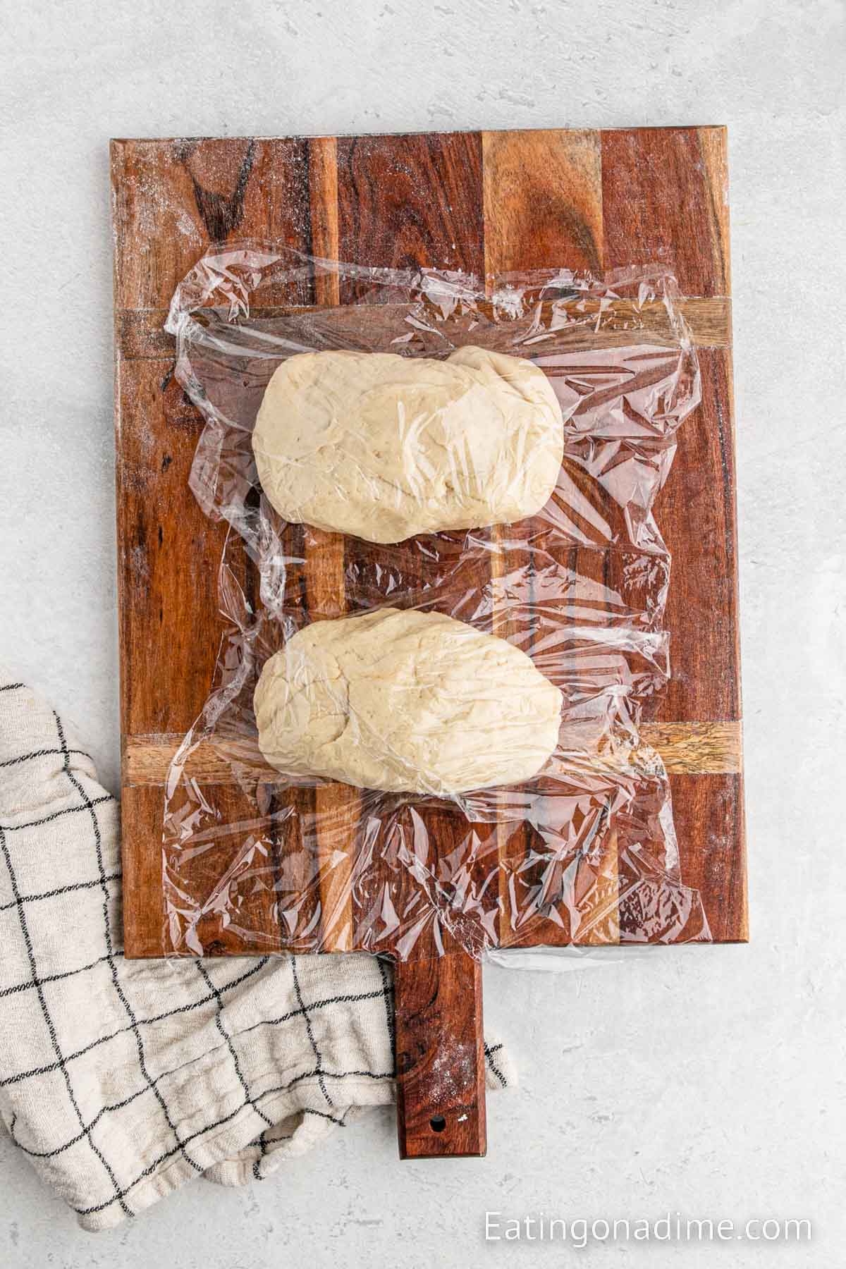 Covering the dough on a cutting board with plastic wrap