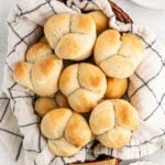 A basket lined with a beige and black striped cloth holds several golden brown, soft cloverleaf rolls. Freshly baked and arranged closely, these treats showcase the perfect result of a Homemade Dinner Rolls Recipe.
