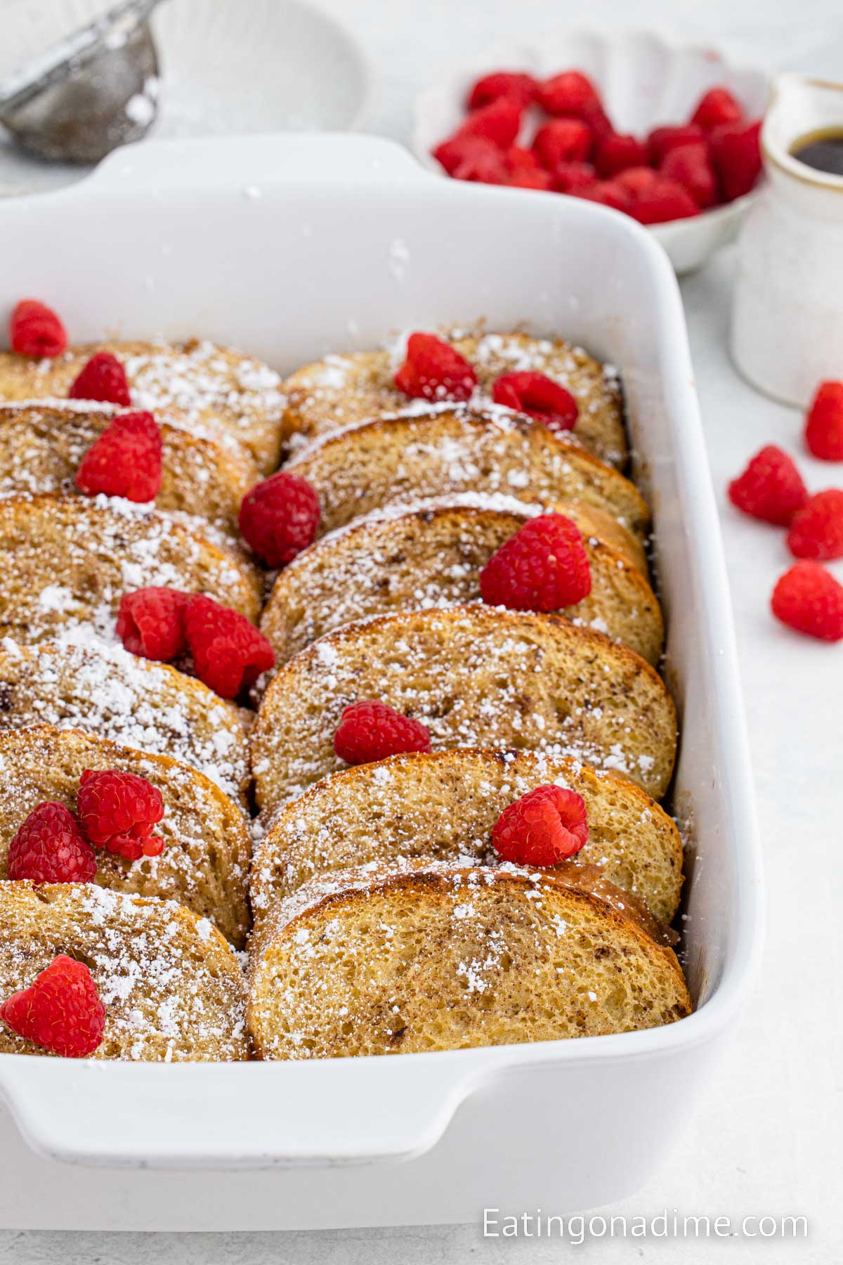 Close up image of French Toast Casserole in a baking dish topped with fresh berries and powdered sugar