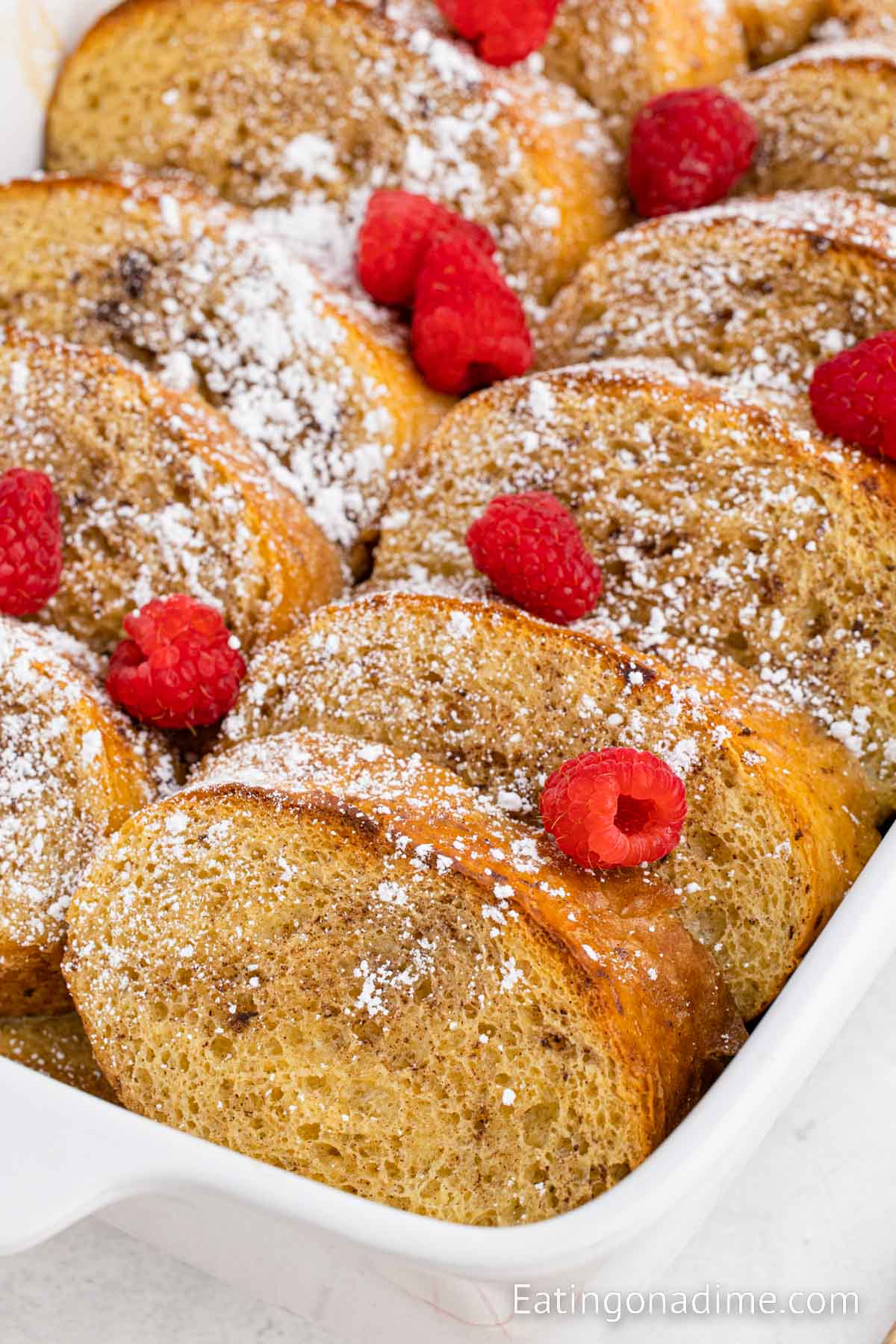 Close up image of French Toast Casserole in a baking dish topped with fresh berries and powdered sugar