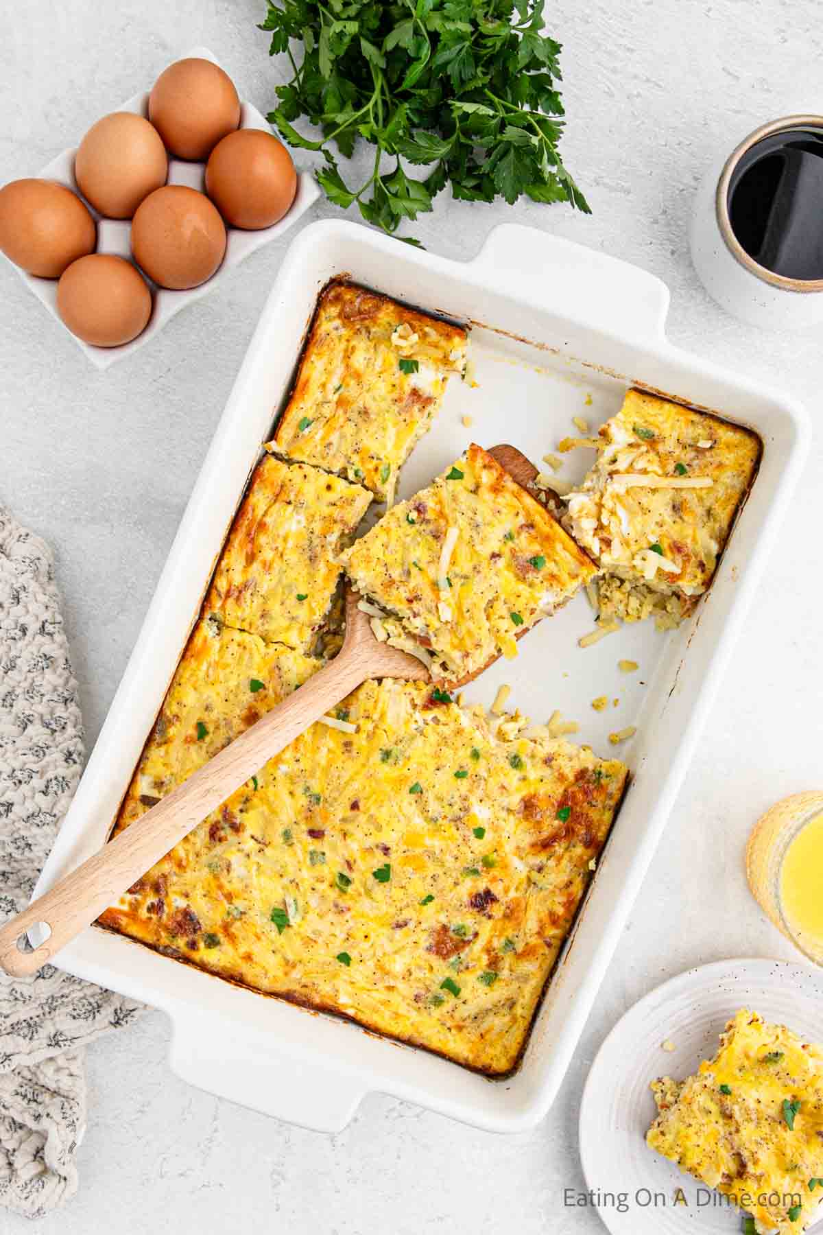 Bacon egg casserole in a baking dish with a serving on a wooden spatula