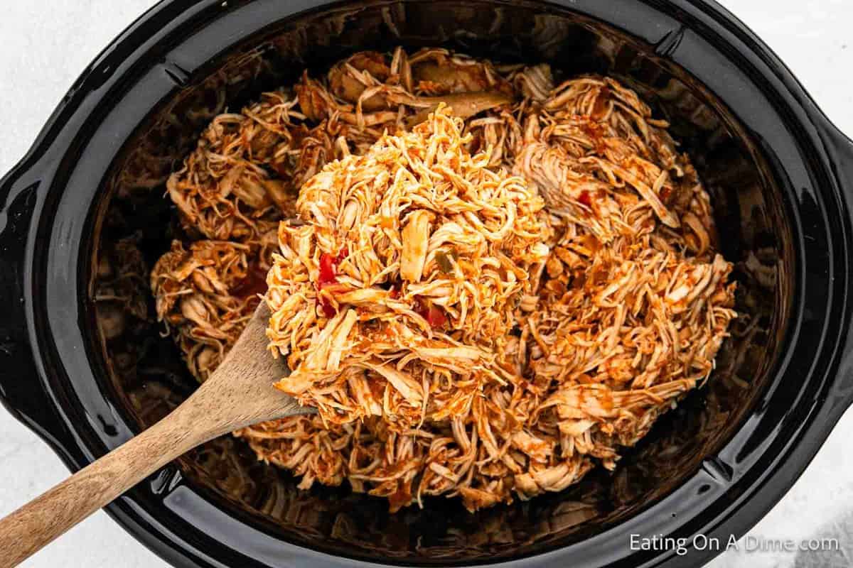 Shredded Salsa Chicken in the crockpot with a serving on a wooden spoon.