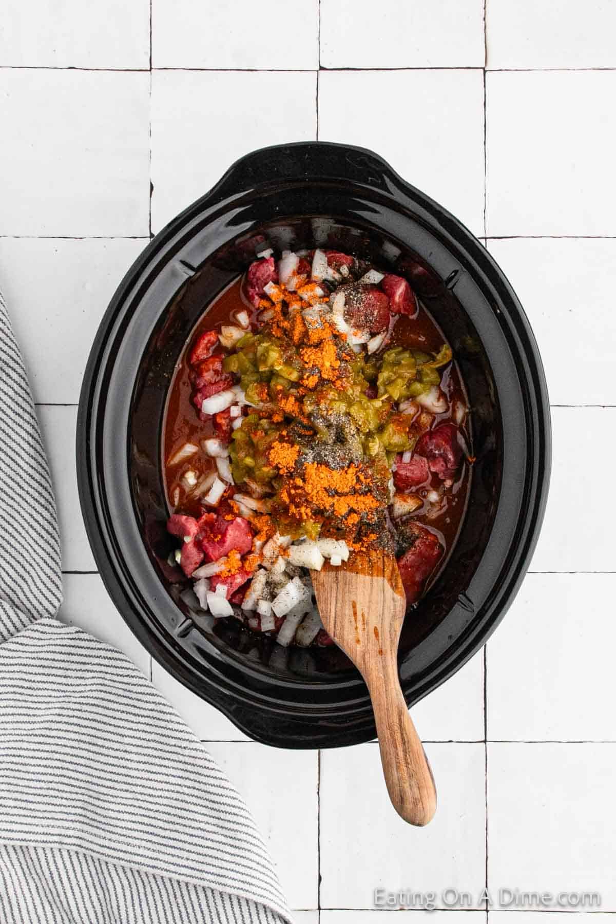 Adding beef stew in the slow cooker with the seasoning, sauce and chopped onions