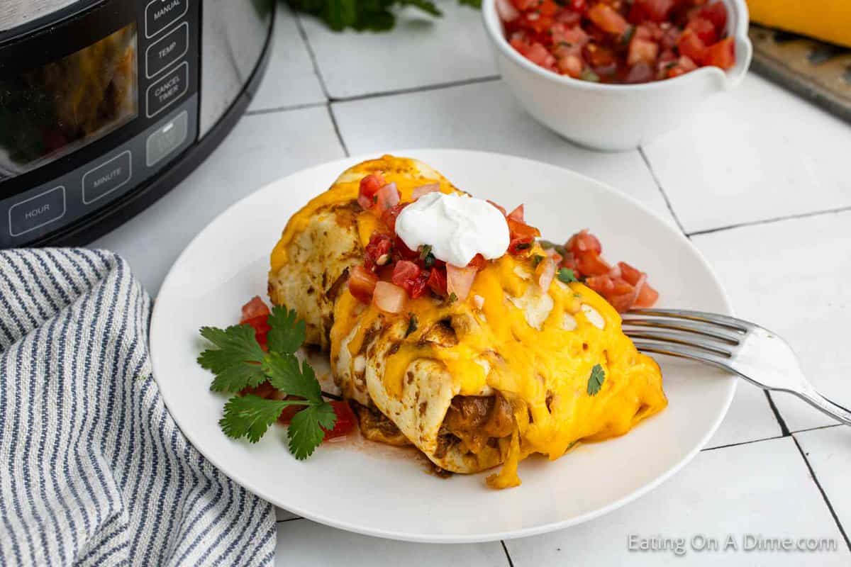 Smothered burritos on a plate topped with pico de gallo and sour cream