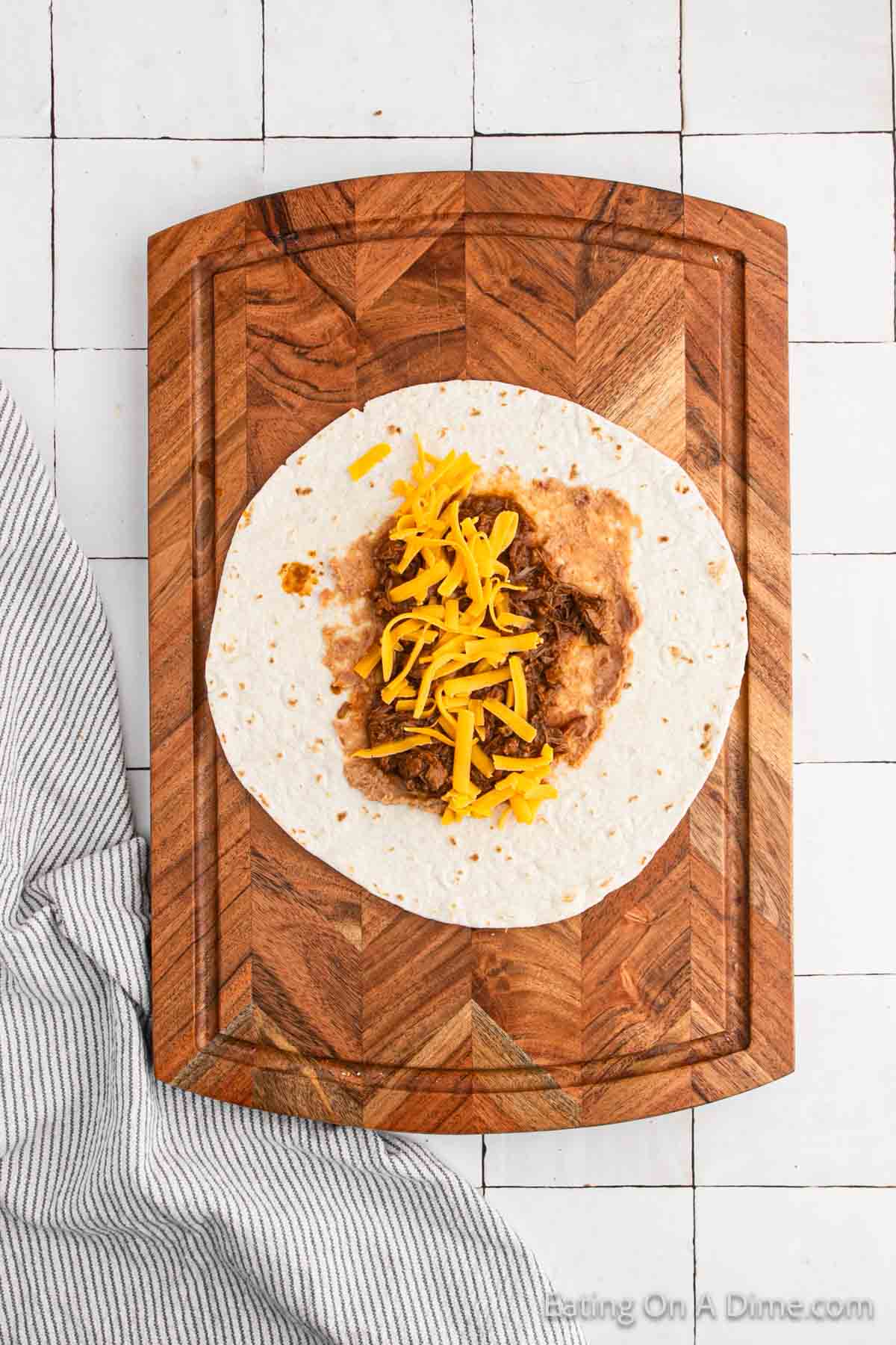 Topping the refried beans on the tortilla with beef mixture and shredded cheese