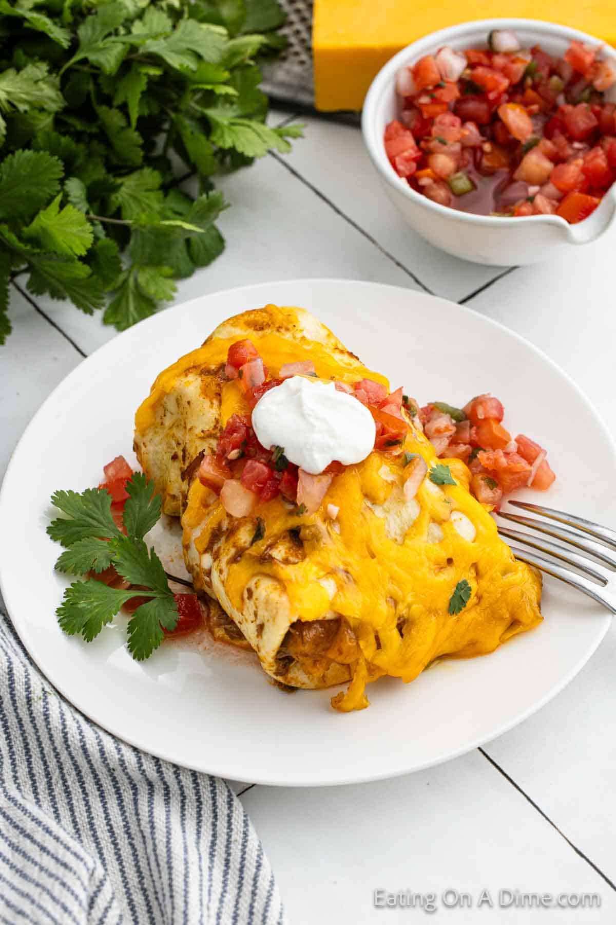 Smothered Burritos on a plate topped with sour cream and pico de gallo