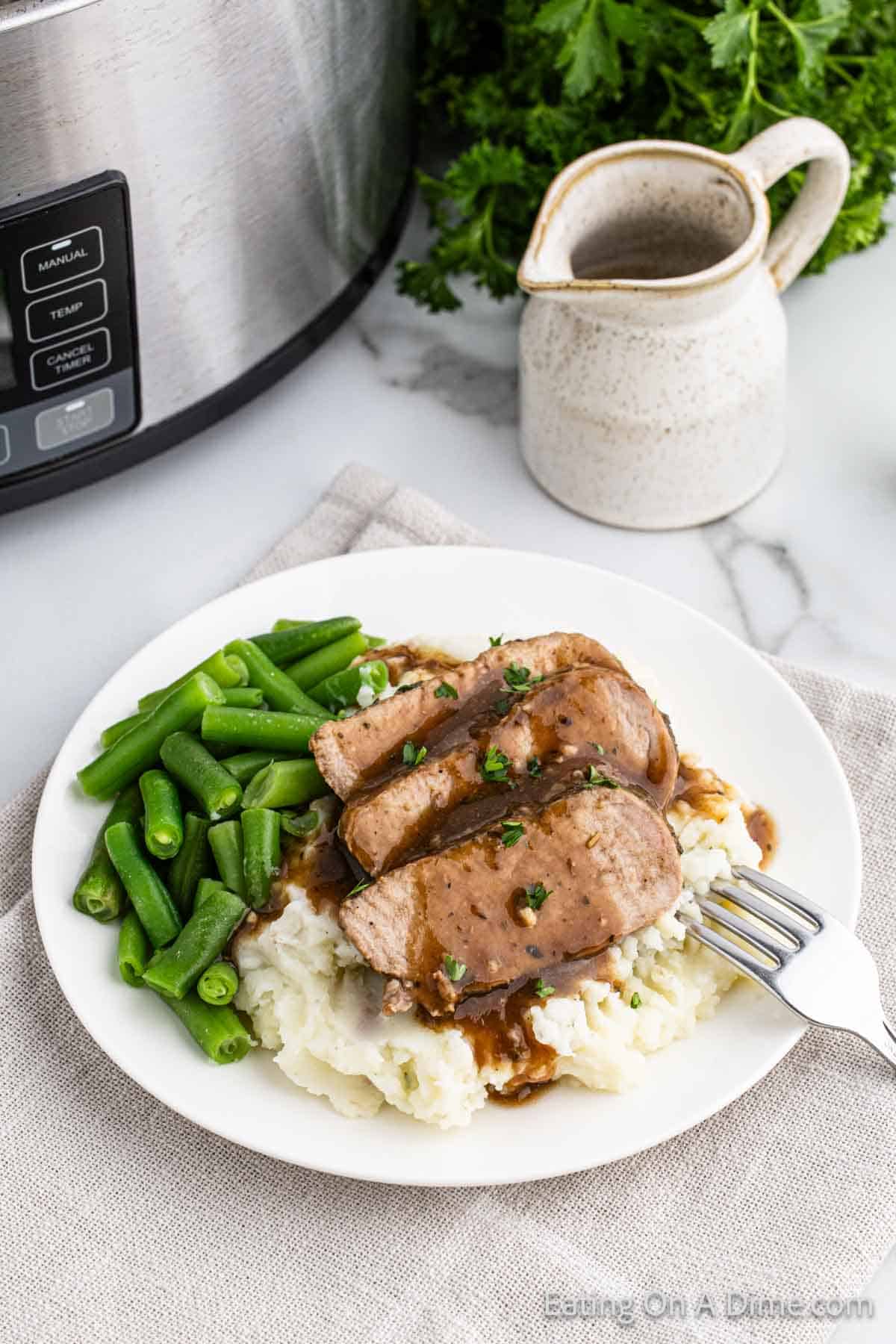Slice pork tenderloin on a plate topped with glaze with green beans and mashed potatoes