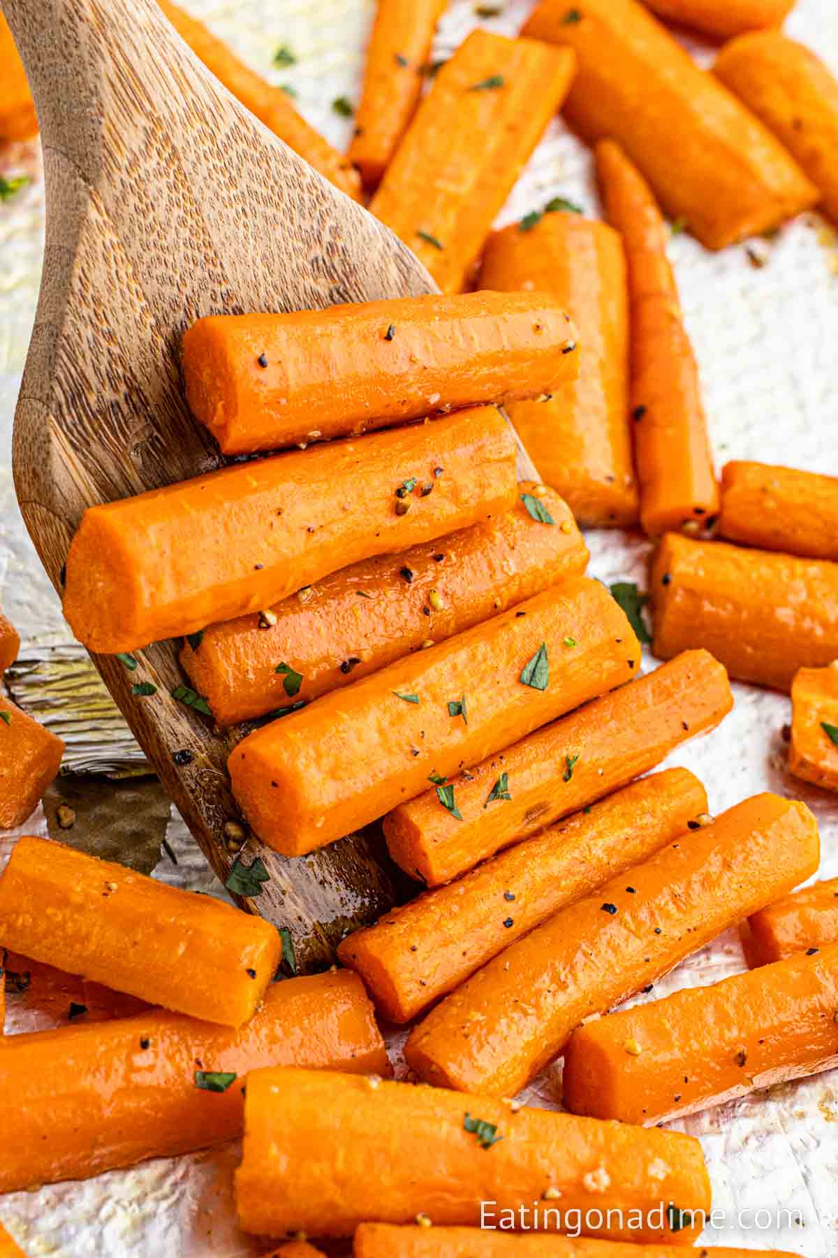 Roasted carrots on a baking sheet with a serving on a wooden spoon