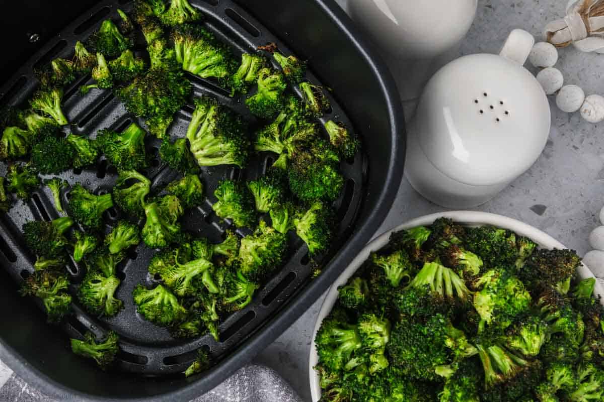 Cooked broccoli in an air fryer basket and in a bowl.