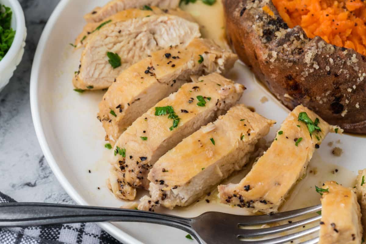 Brown Sugar Chicken sliced on a plate with a sweet potato on the side.