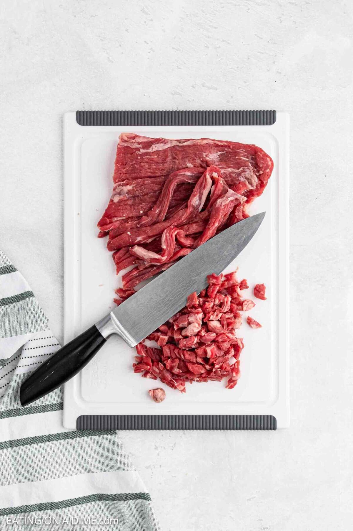 Chopping and slicing flank steak with a knife on a cutting board.