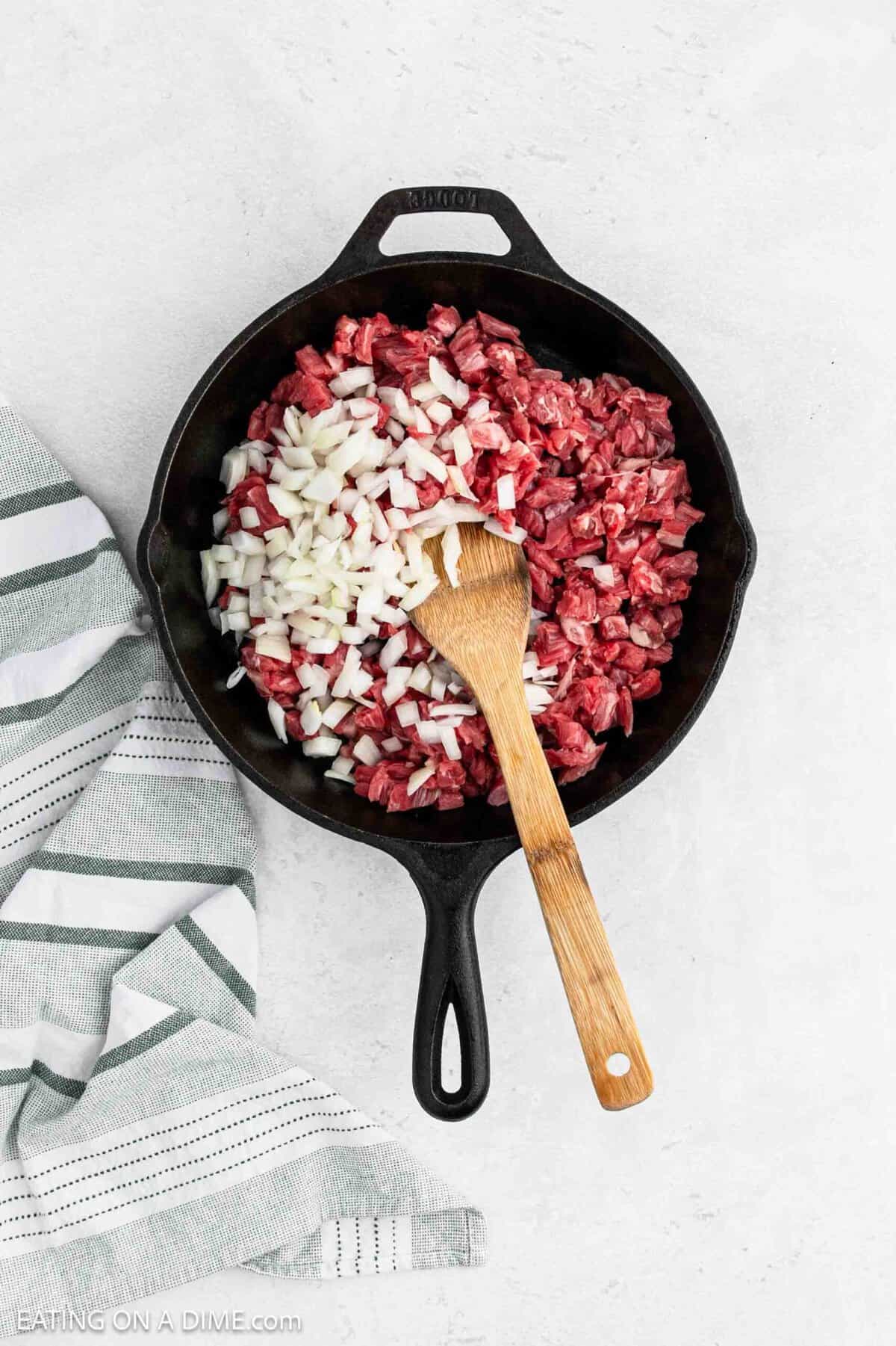 Cooking chopped flank steak in a cast iron skillet topped with chopped onions.