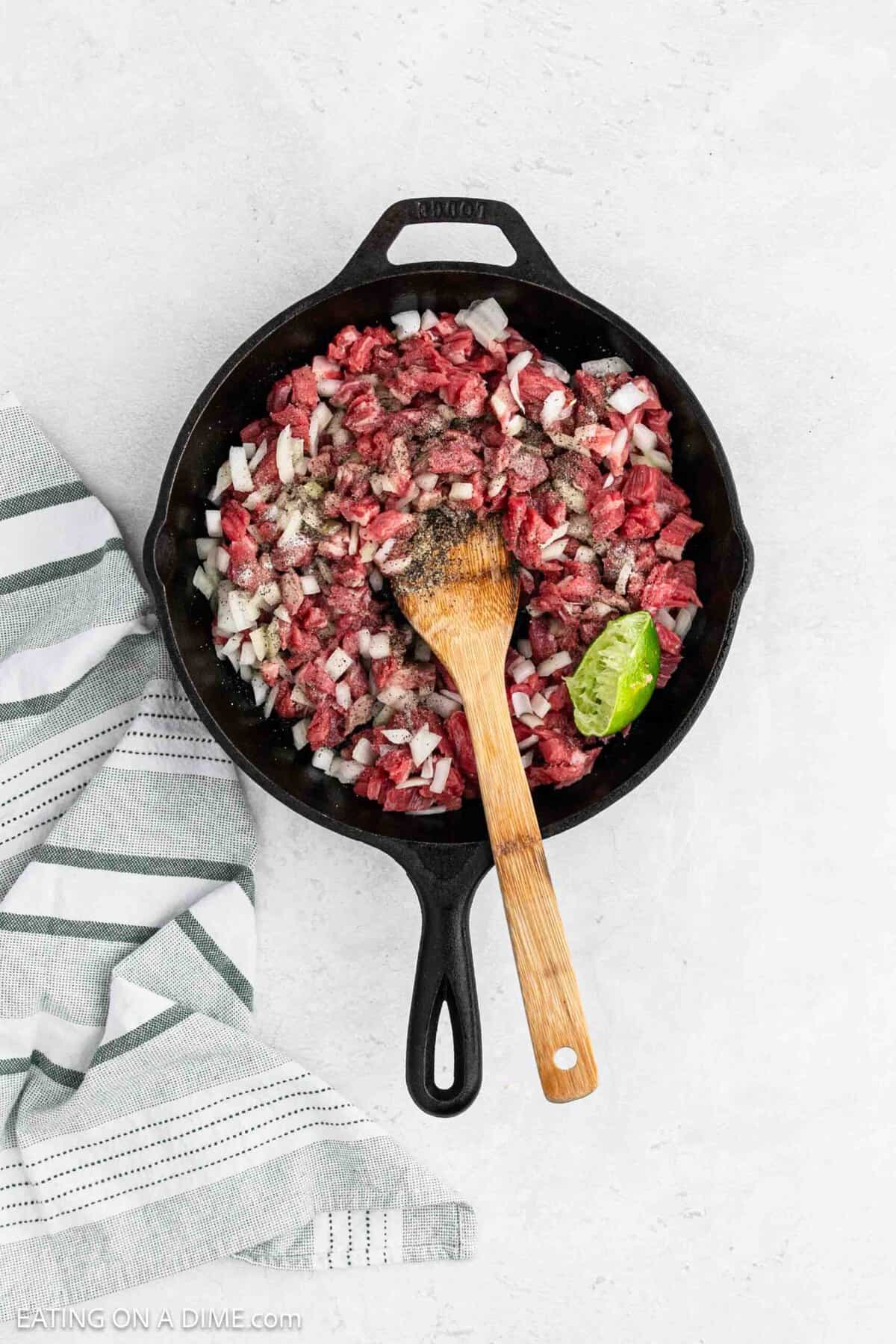 Chopped flank steak in a cast iron skillet mixed with chopped onions topped with seasoning and fresh lime.