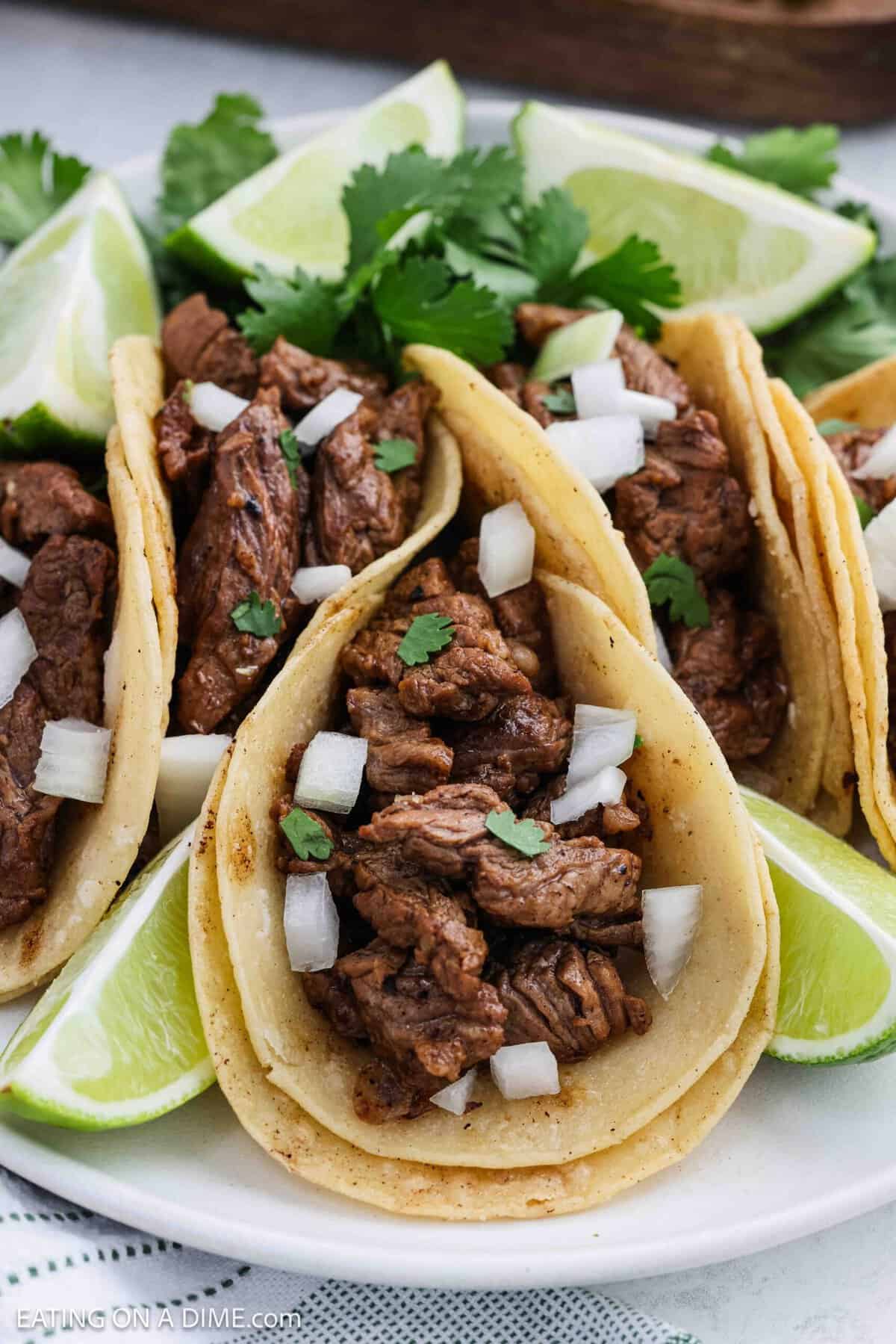Close up image of steak tacos on a plate topped with chopped onions and cilantro.