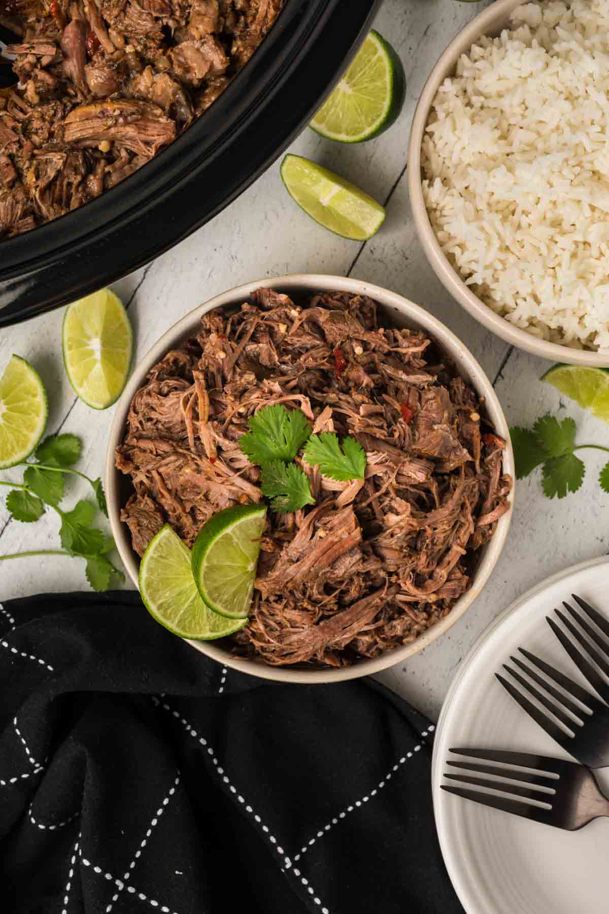 Shredded beef in a bowl with lime wedges and a bowl of white rice on the side